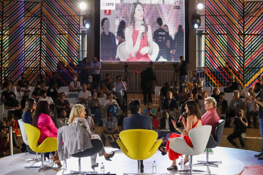Imagem da Virada ODS 2022 durante um painel com várias pessoas assistindo e um grupo de pessoas no palco apresentando